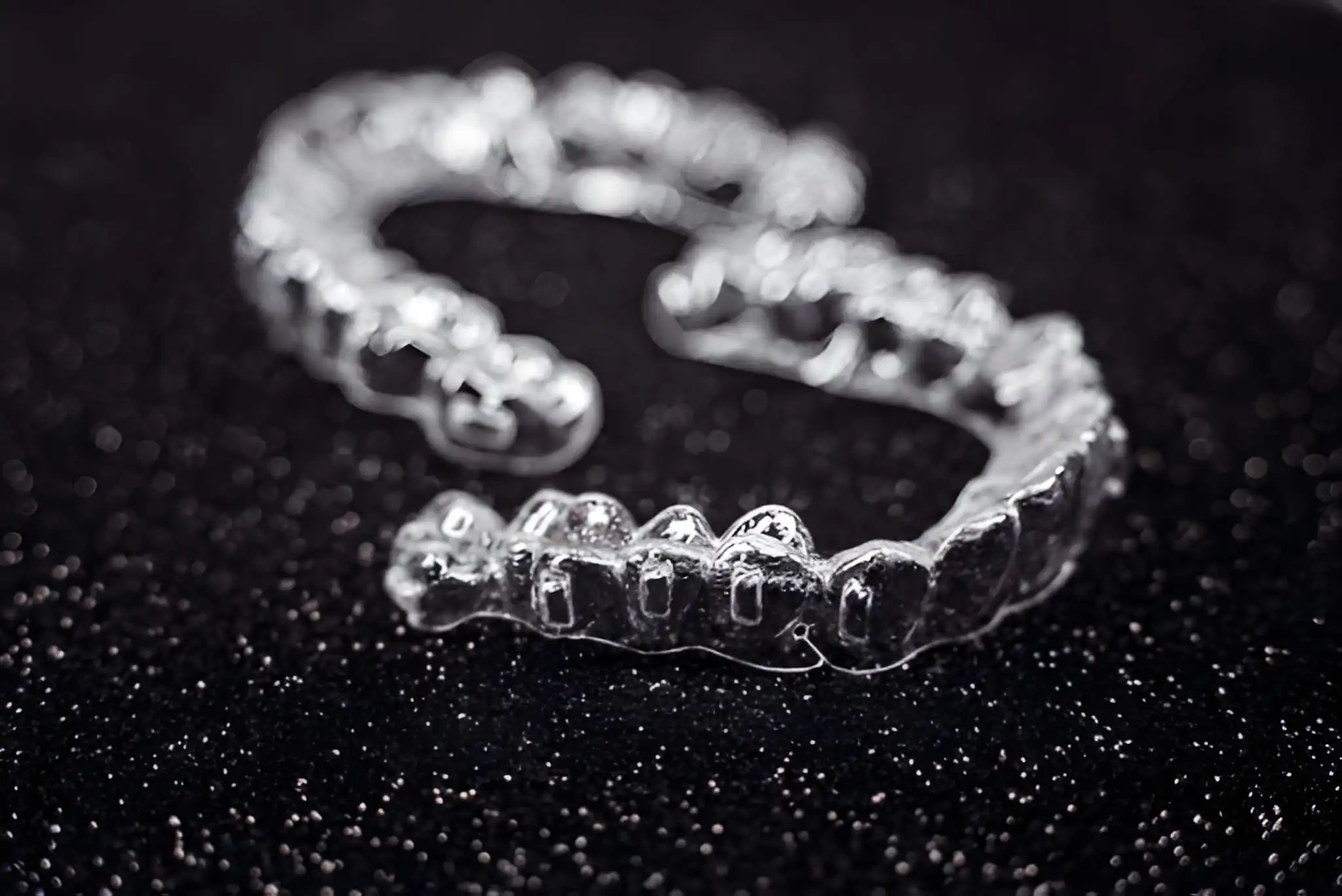 Retainers for teeth in Flower Mound TX clear aligner trays displayed on black background at Supreme Smiles Dentistry.